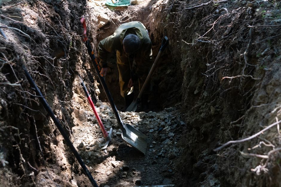 A person digging a trench outside, surrounded by tools and natural surroundings.